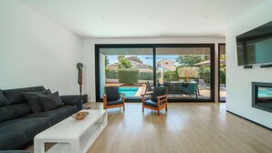 A modern living room with a black sofa, white coffee table, and wooden chairs. A large glass door leads to an outdoor pool area. - V. Ca Na Rosa With Private Pool (Mal Pas - Bon Aire)