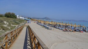 A beach with a wooden boardwalk leading to the shore, rows of beach umbrellas, and a clear view of the sea and distant mountains. - V. Ca Na Rosa With Private Pool (Mal Pas - Bon Aire)