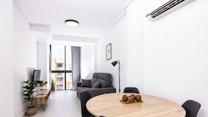 A modern living room with a round wooden table, black chairs, a grey sofa, and a floor lamp. - Apartamentos Marina Playa de Torrevieja (Torrevieja)