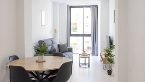 A modern living room with a round wooden table, grey sofa, and a large window with curtains. - Apartamentos Marina Playa de Torrevieja (Torrevieja)