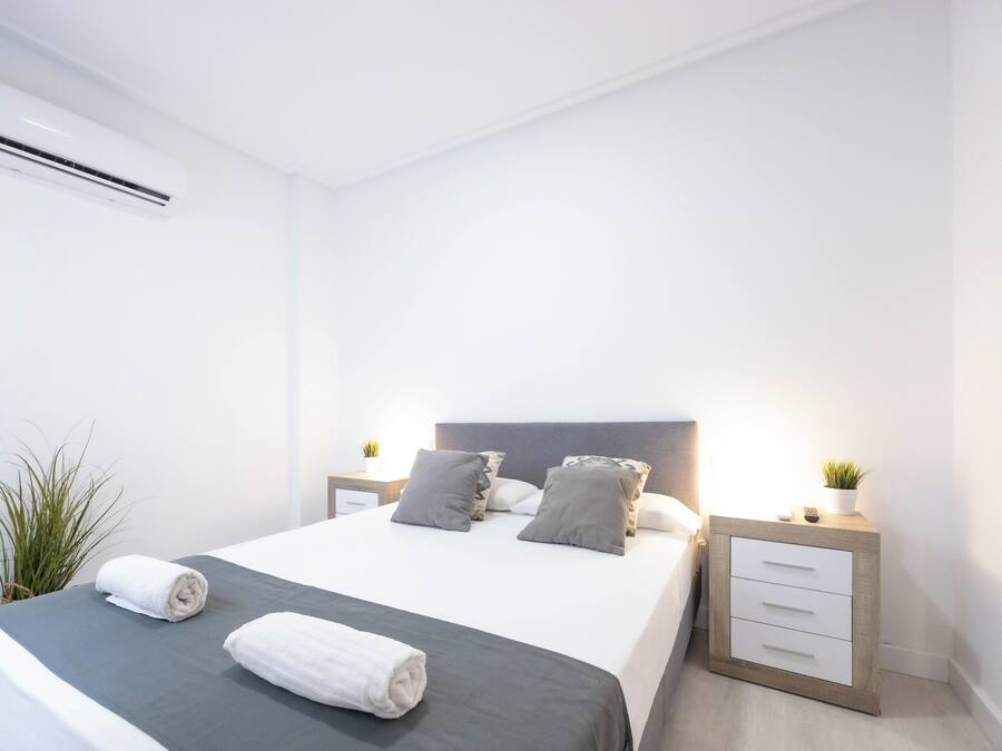 A modern hotel room with a neatly made bed, a bedside table with a lamp, and a small plant on the nightstand.