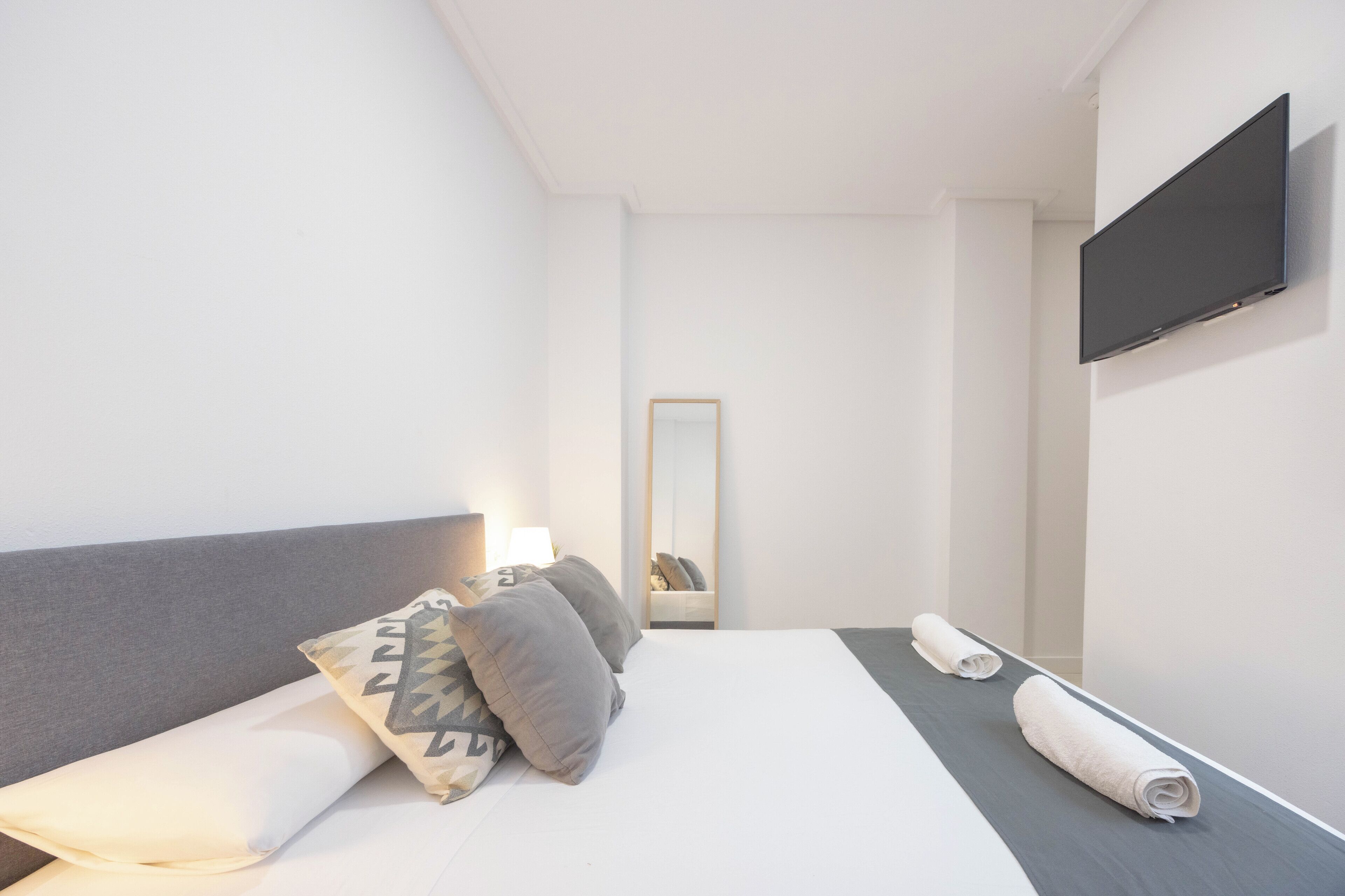 Une chambre d’hôtel moderne, équipée d’un lit, d’un téléviseur à écran plat fixé au mur et d’un miroir qui reflète la pièce.