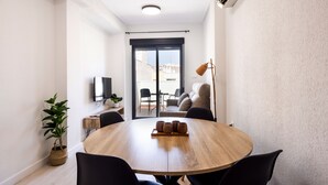 A modern, well-lit room with a round wooden table, black chairs, a potted plant, and a television on the wall. - Apartamentos Marina Playa de Torrevieja (Torrevieja)