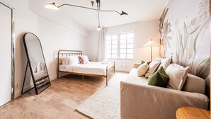 Een slaapkamer met een bed, een spiegel, een raam, een lamp en een bank.