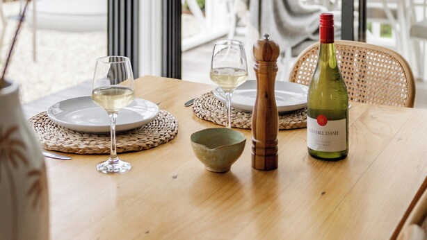A dining table set with a bottle of wine, glasses, a bowl, and a pepper mill.