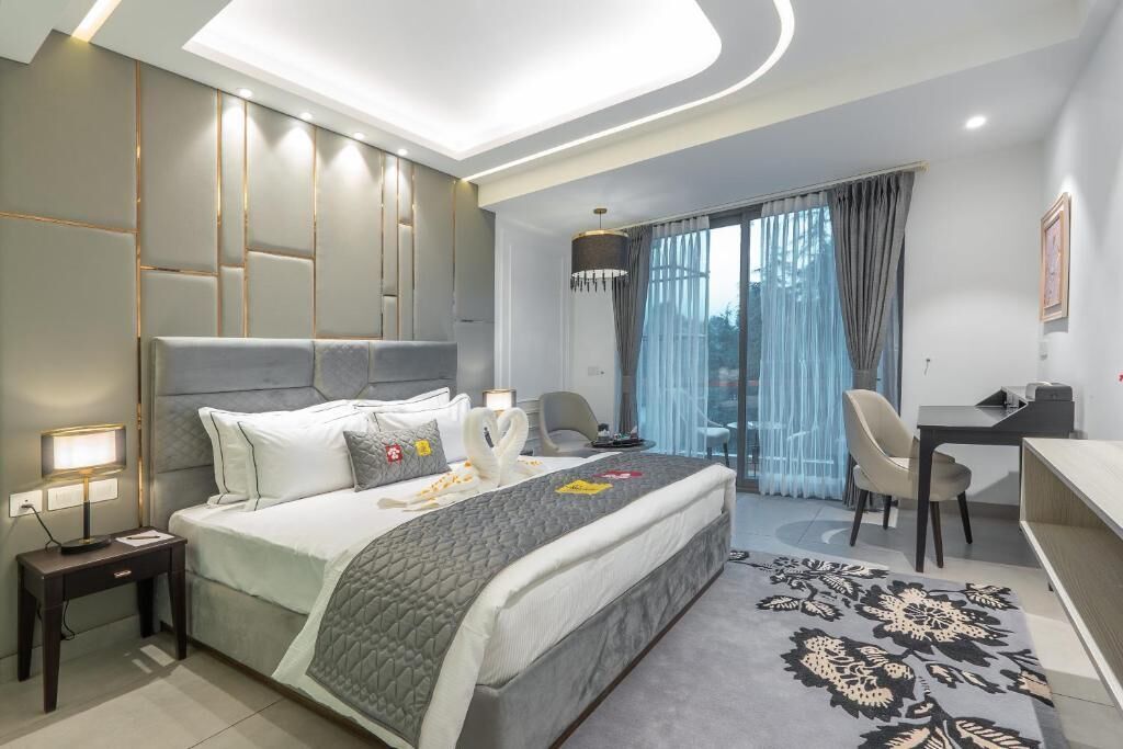 A modern hotel room with a large bed, a desk, a chair, and a view of the outdoors.