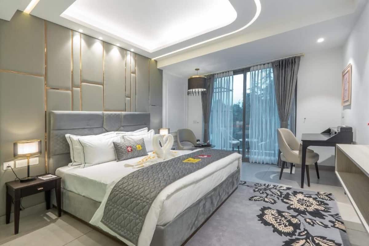 A modern hotel room with a large bed, a desk, a chair, and a view of the outdoors.
