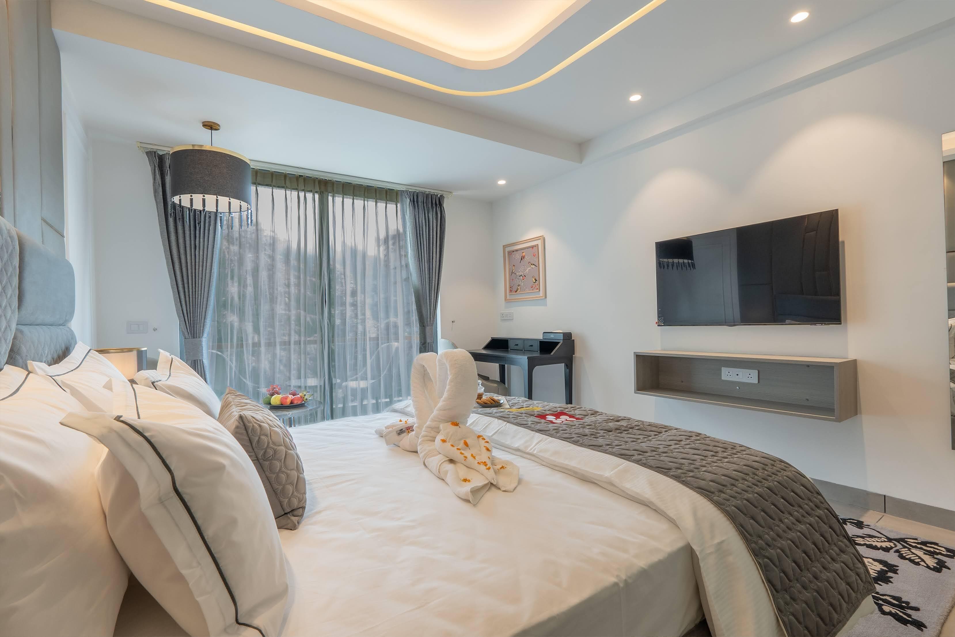 A modern hotel room with a neatly made bed, a desk, a flat-screen TV, and a large window with curtains.
