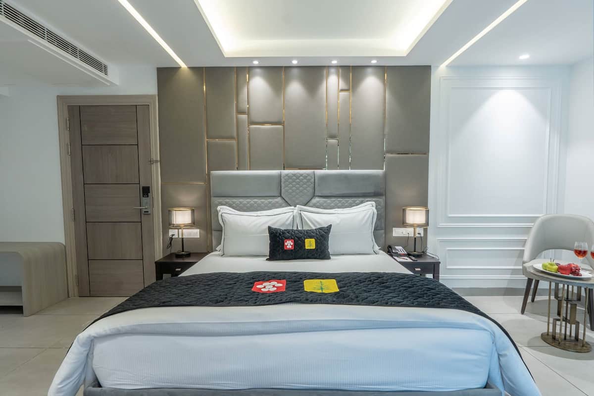 A modern hotel room with a large bed, bedside lamps, a small table with fruit, and a chair.