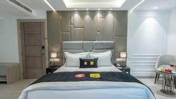 A modern hotel room with a large bed, bedside lamps, a small table with fruit, and a chair.