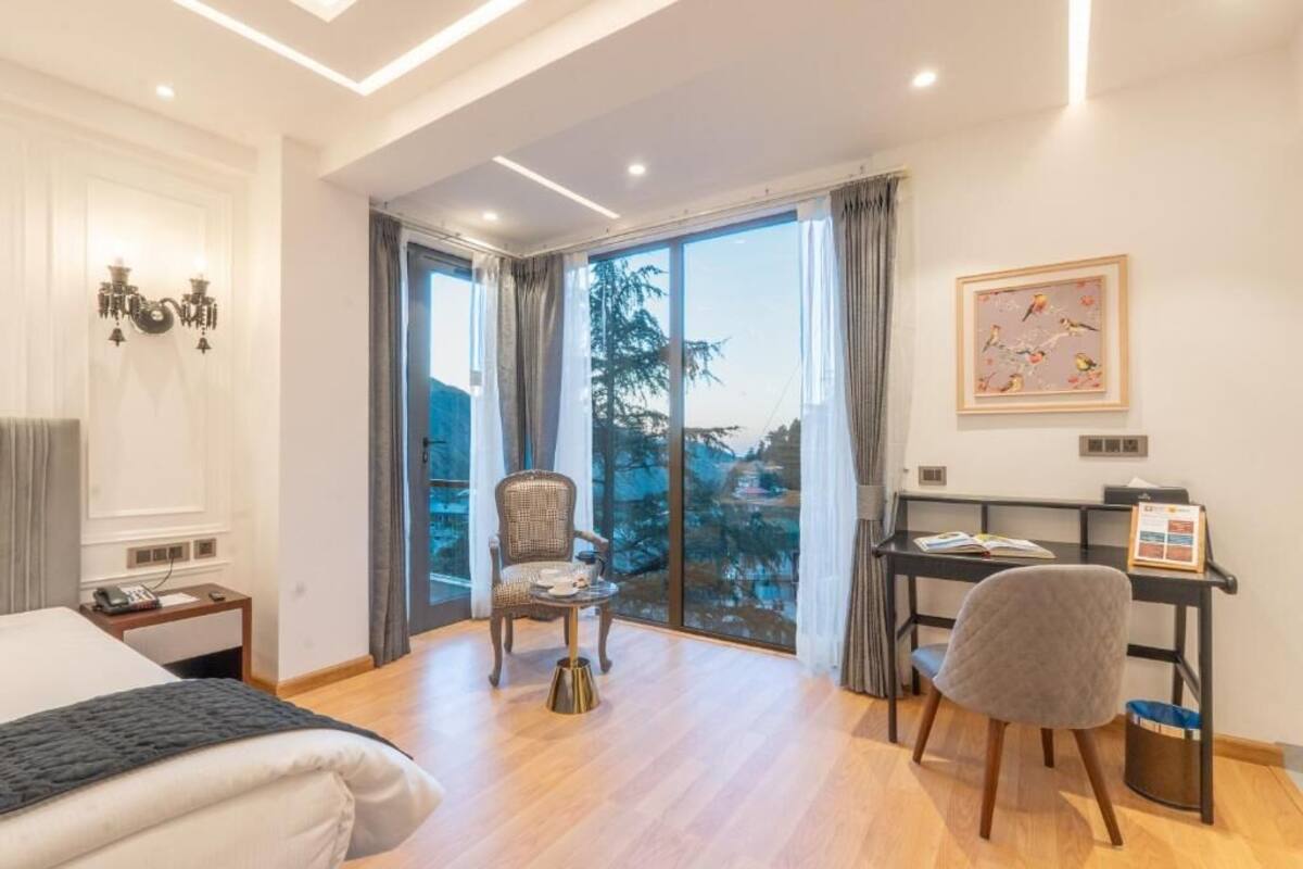 A hotel room with a bed, a desk, a chair, a small table, and a view of the outdoors.