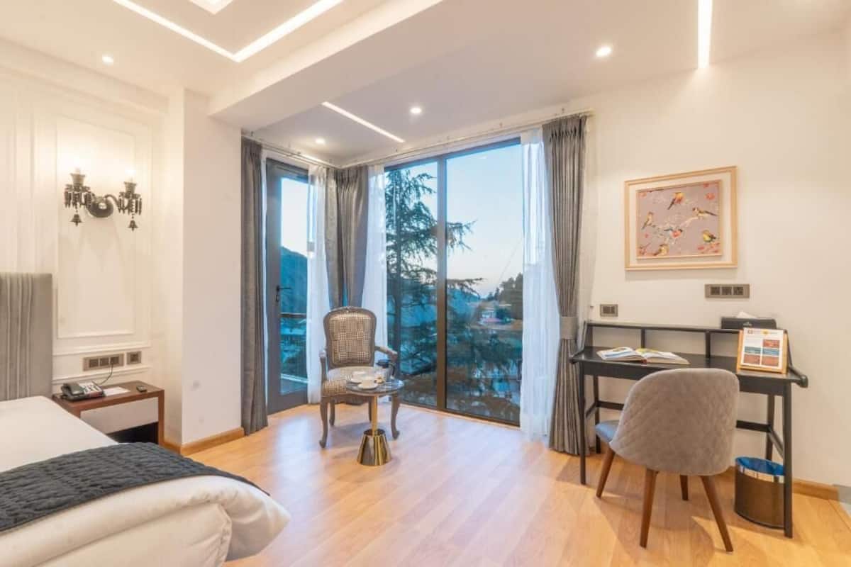 Ein Hotelzimmer mit Bett, Schreibtisch, Stuhl, einem kleinen Tisch und Blick ins Freie.
