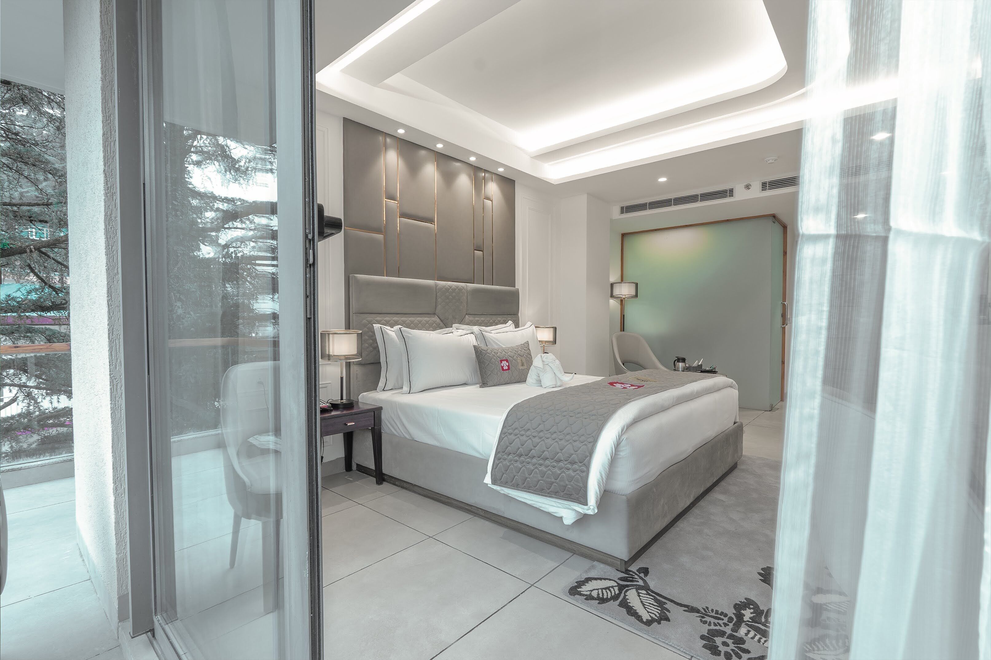 Ein modernes Schlafzimmer mit einem großen Bett, Nachttischen und Blick durch eine Glastür.