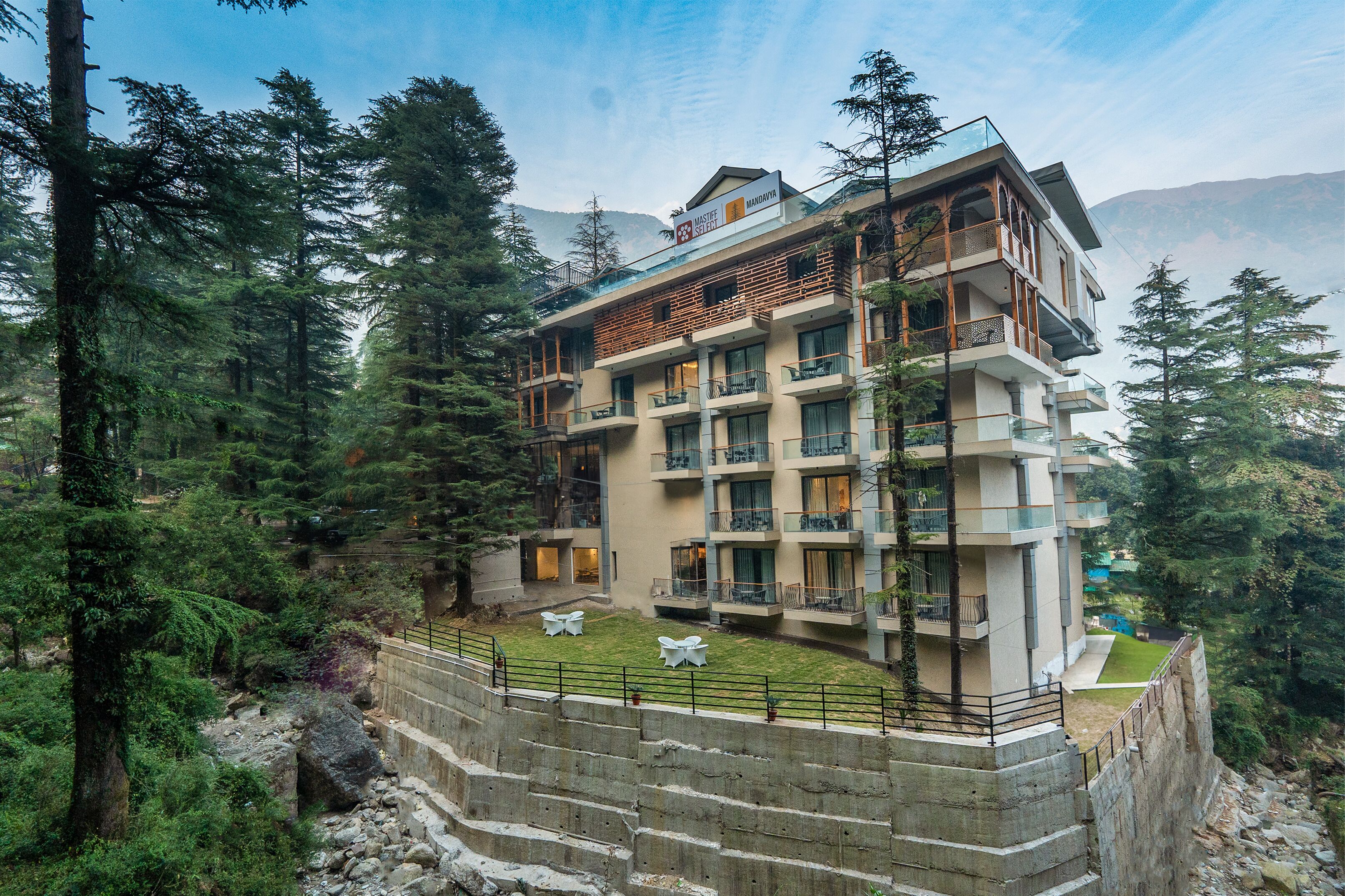 Un hôtel à plusieurs étages, doté de balcons et entouré de montagnes boisées.