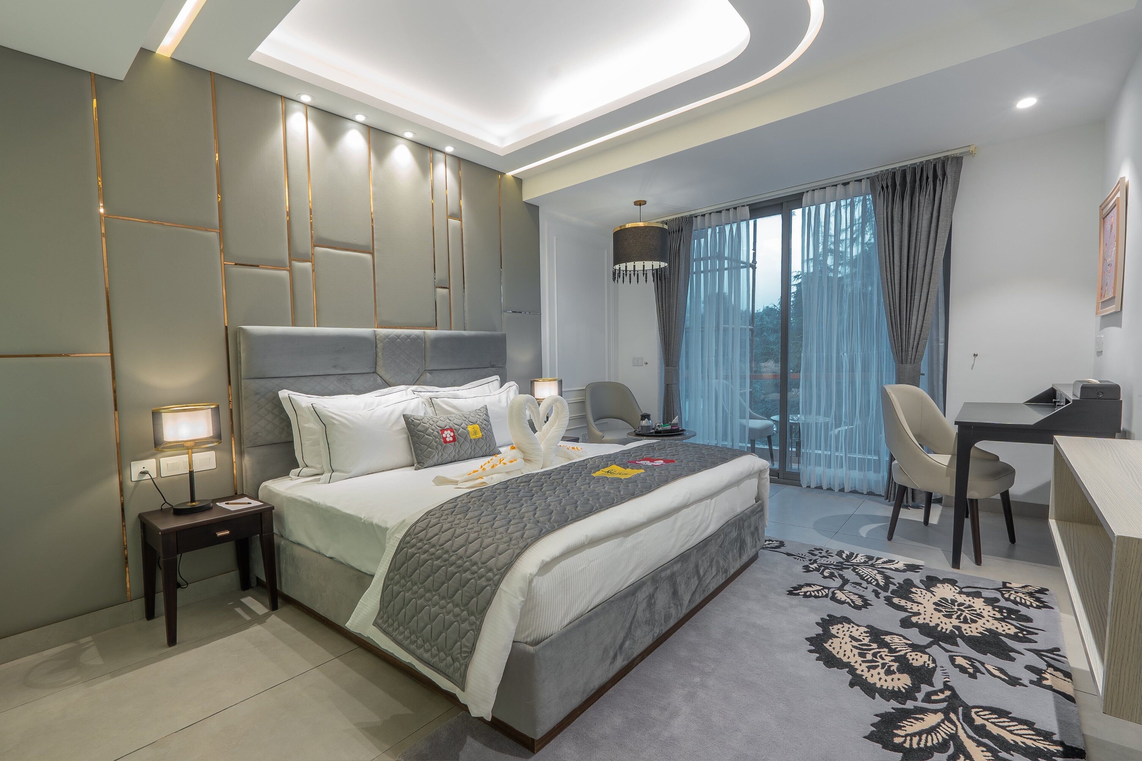 A modern hotel room with a large bed, a desk, and a view of the outdoors.