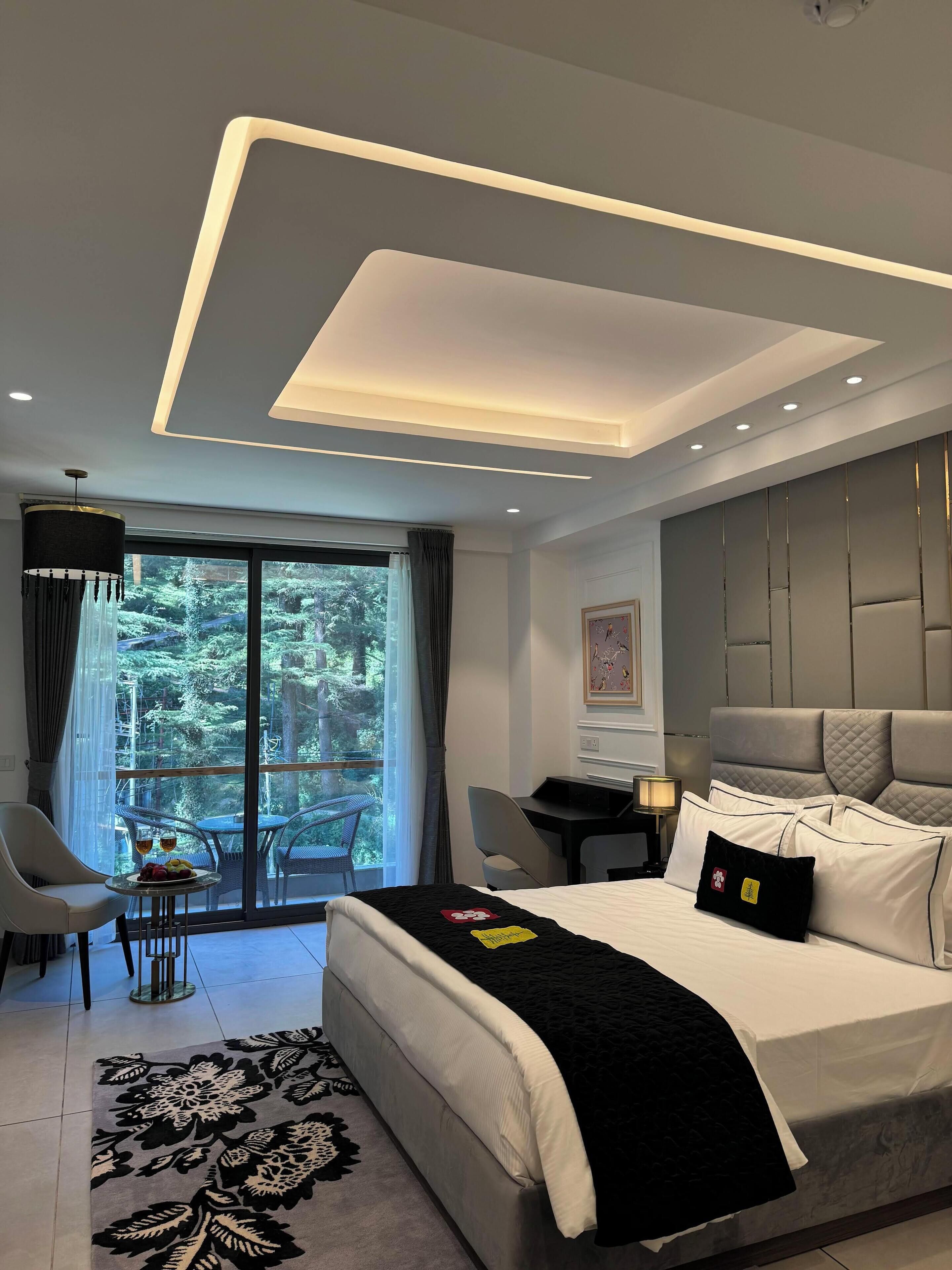 A modern hotel room with a large bed, a desk, and a view of a forest through the window.