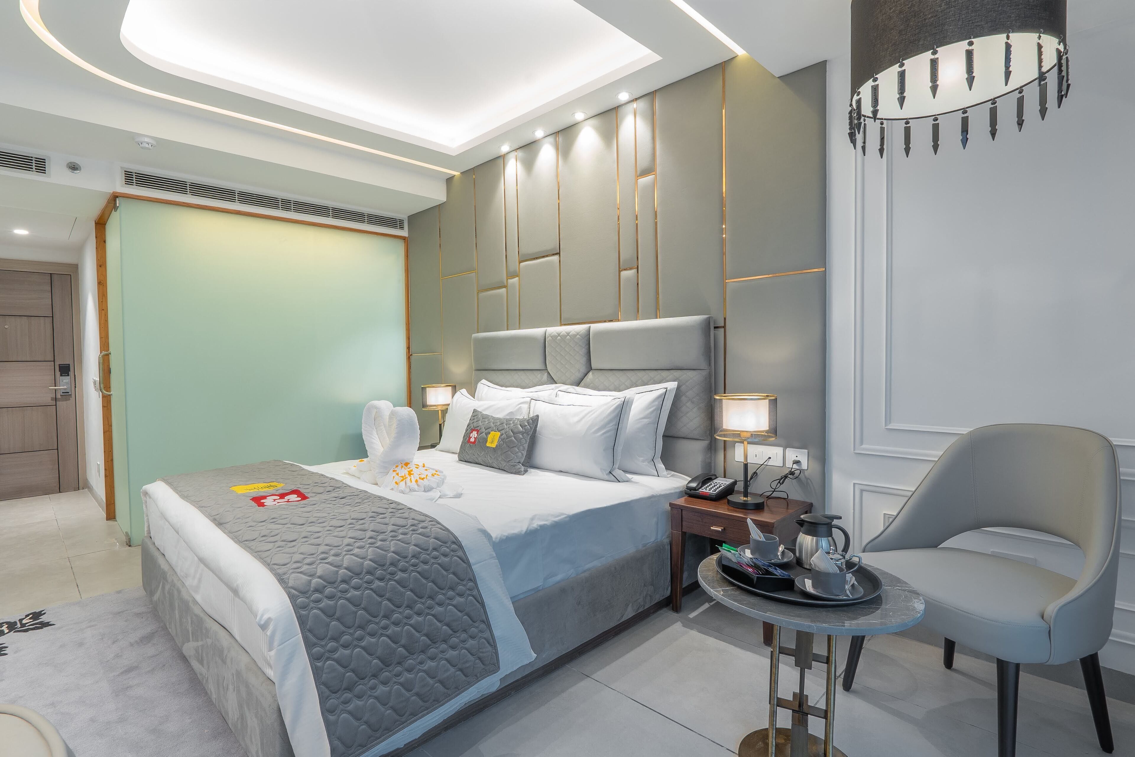 Une chambre d’hôtel moderne avec un grand lit, des tables de chevet, une chaise et une petite table avec un plateau.