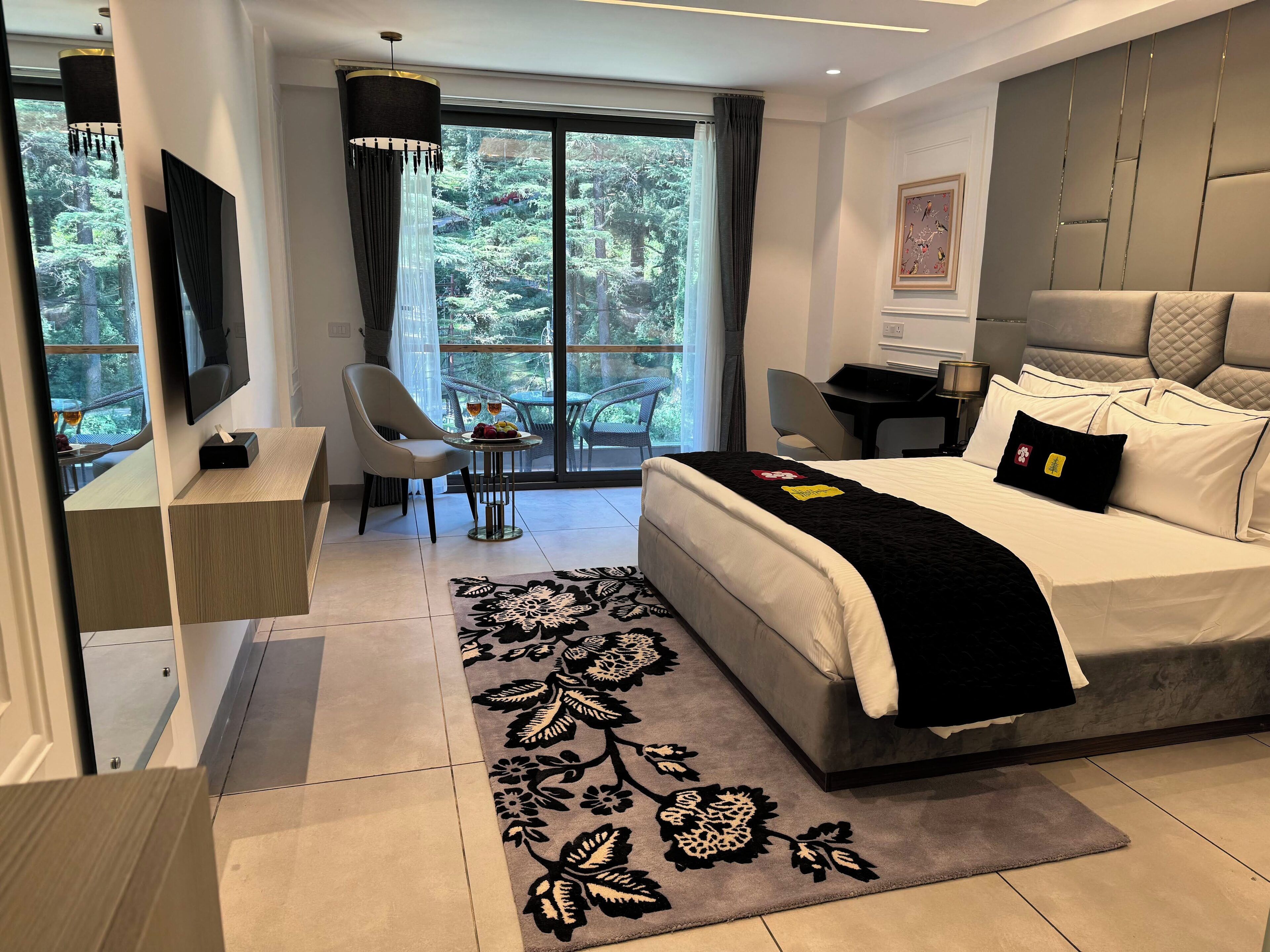 Ein modernes Hotelzimmer mit einem großen Bett, einem Schreibtisch, einem Sessel und Blick ins Freie.