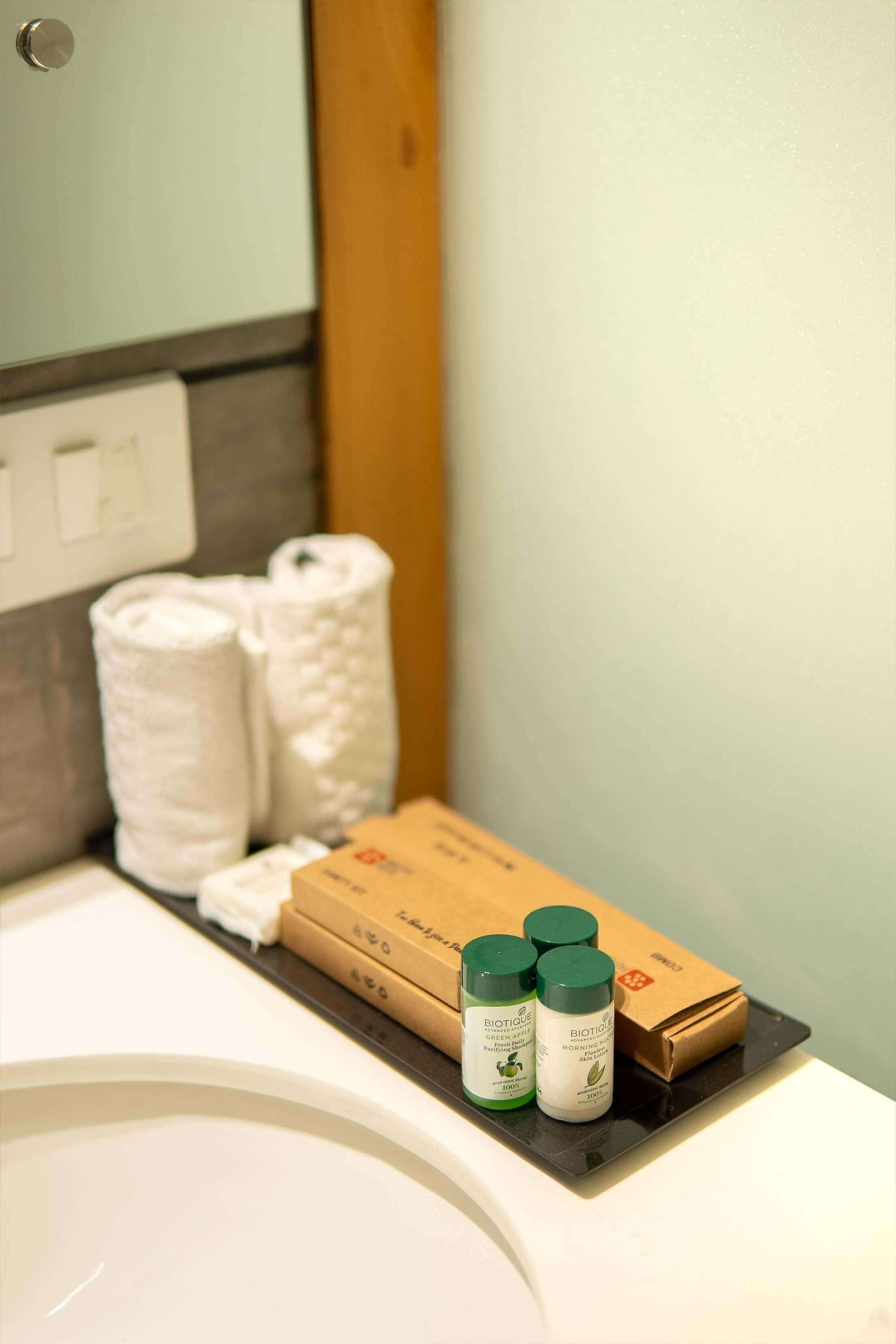 A bathroom with a sink, two rolled towels, and three Biotique products on the counter.