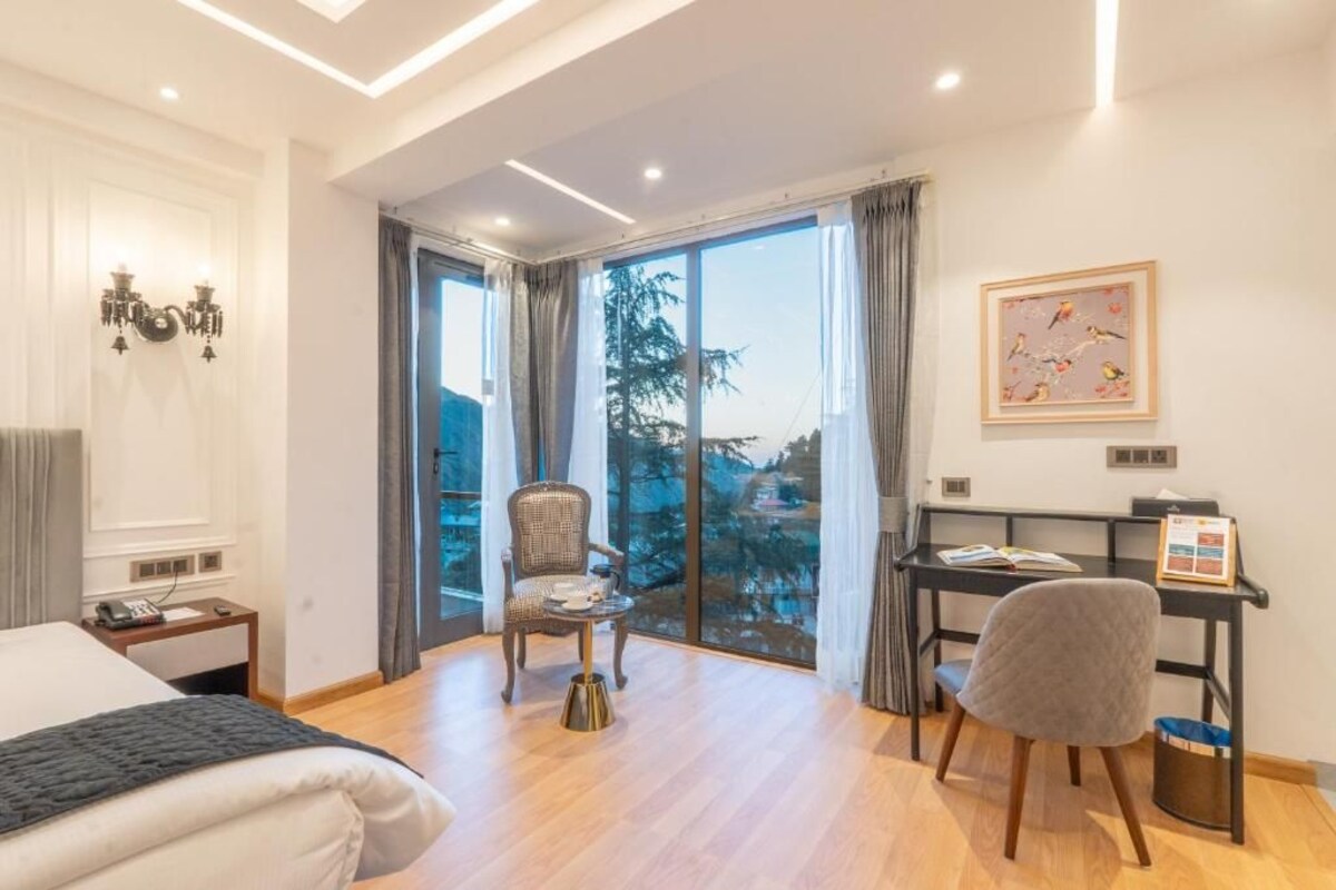 A hotel room with a bed, a desk, a chair, a small table, and a view of the outdoors.
