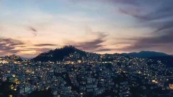 A cityscape at dusk with a densely packed urban area and a hill in the background.