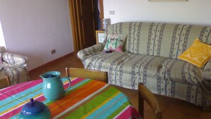 Ein Wohnzimmer mit einer Couch, einer bunten Tischdecke mit Streifen und einem Krug auf dem Tisch.