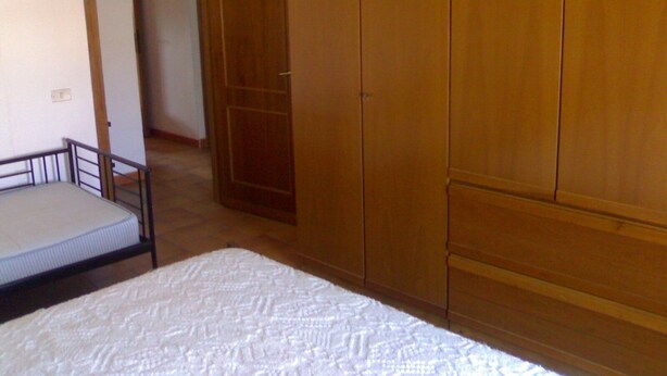Ein Schlafzimmer mit einem Bett, einem Kleiderschrank und einer Tür zu einem weiteren Raum.