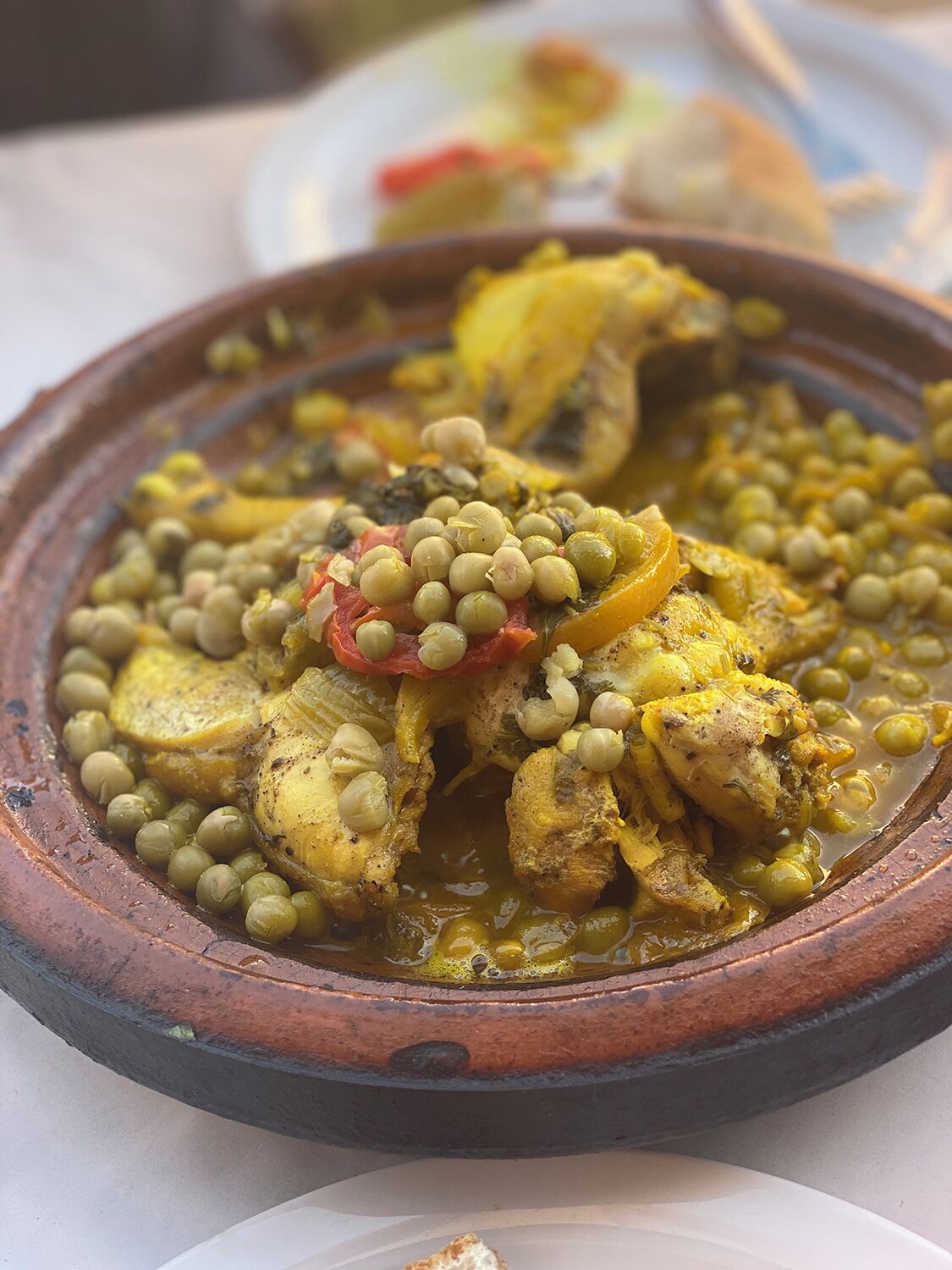 Una olla de barro tradicional llena de un guiso con pollo, guisantes y tomates.