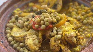 Una olla de barro tradicional llena de un guiso con pollo, guisantes y tomates.
