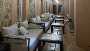 Un corridoio con divani e tavoli, pareti in pietra, travi a vista in legno e lampade a sospensione.