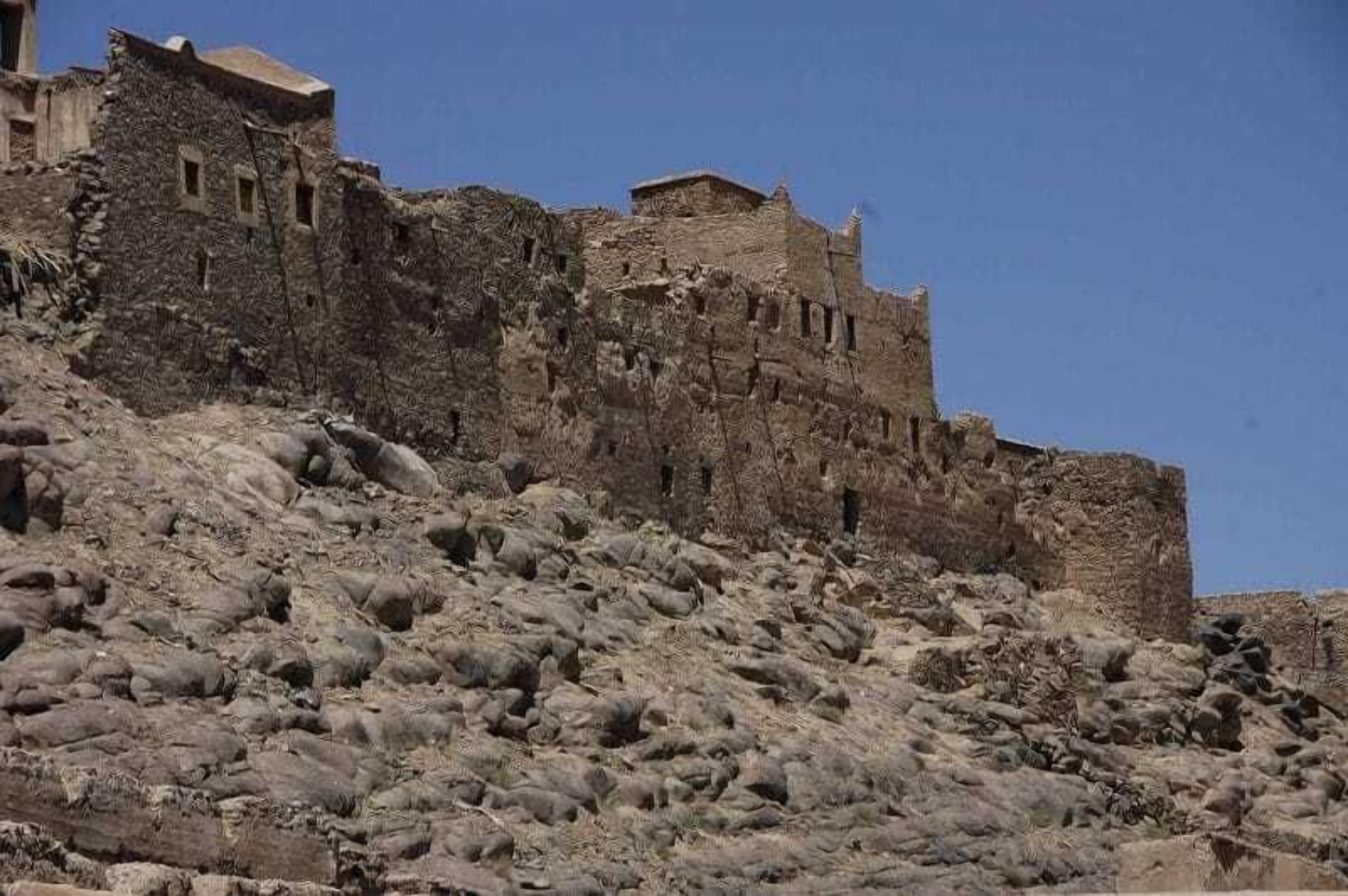 Une forteresse ancienne et imposante, construite en pierre brute, dotée de plusieurs niveaux et de fenêtres étroites, et entourée d’un paysage rocheux.