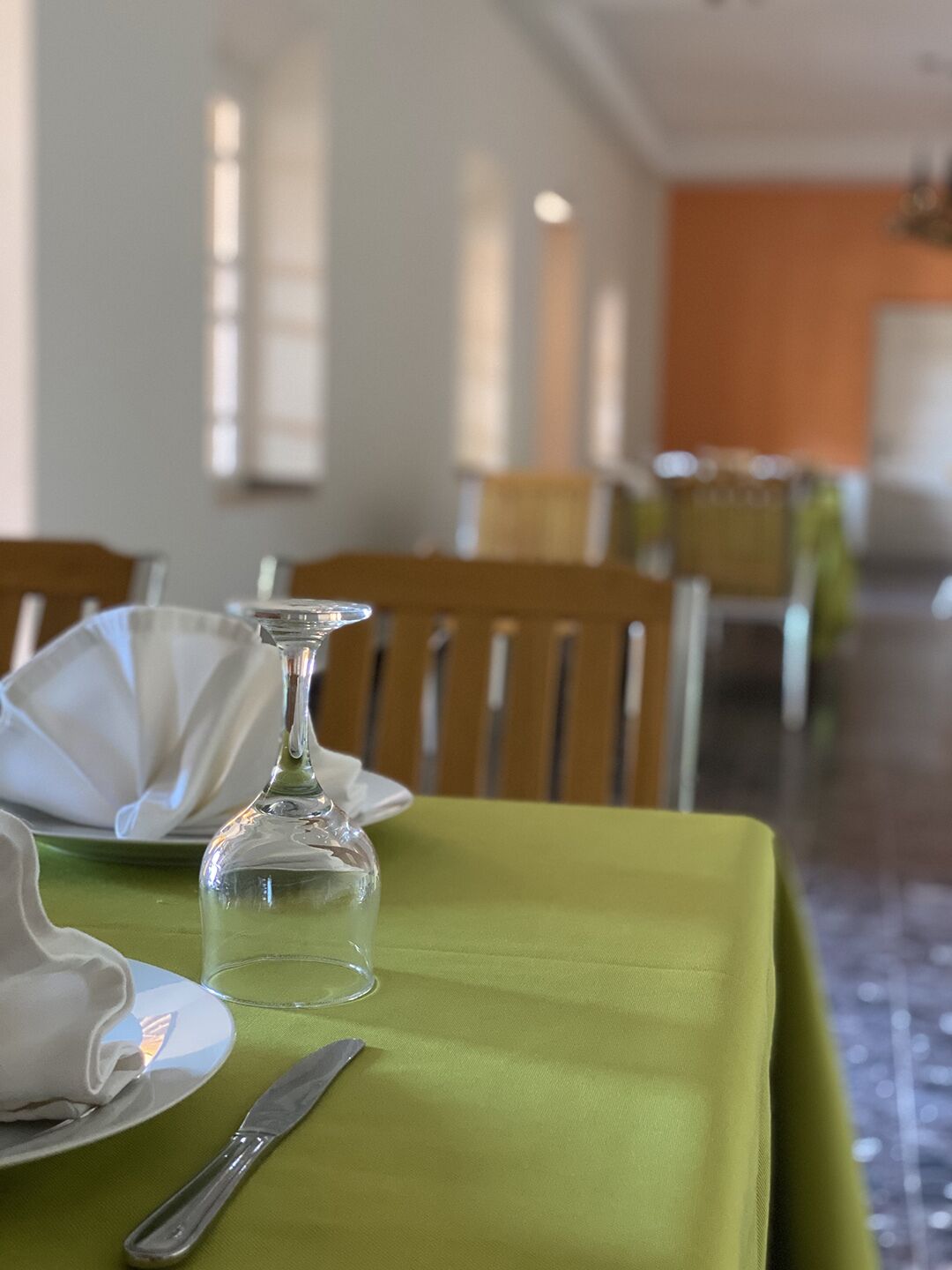 Una mesa de comedor dispuesta con mantel verde, platos blancos, una copa y un tenedor de plata.