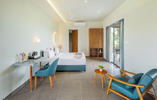 A modern hotel room with a bed, a desk with a chair, a small table with a plant, and a balcony with a view.