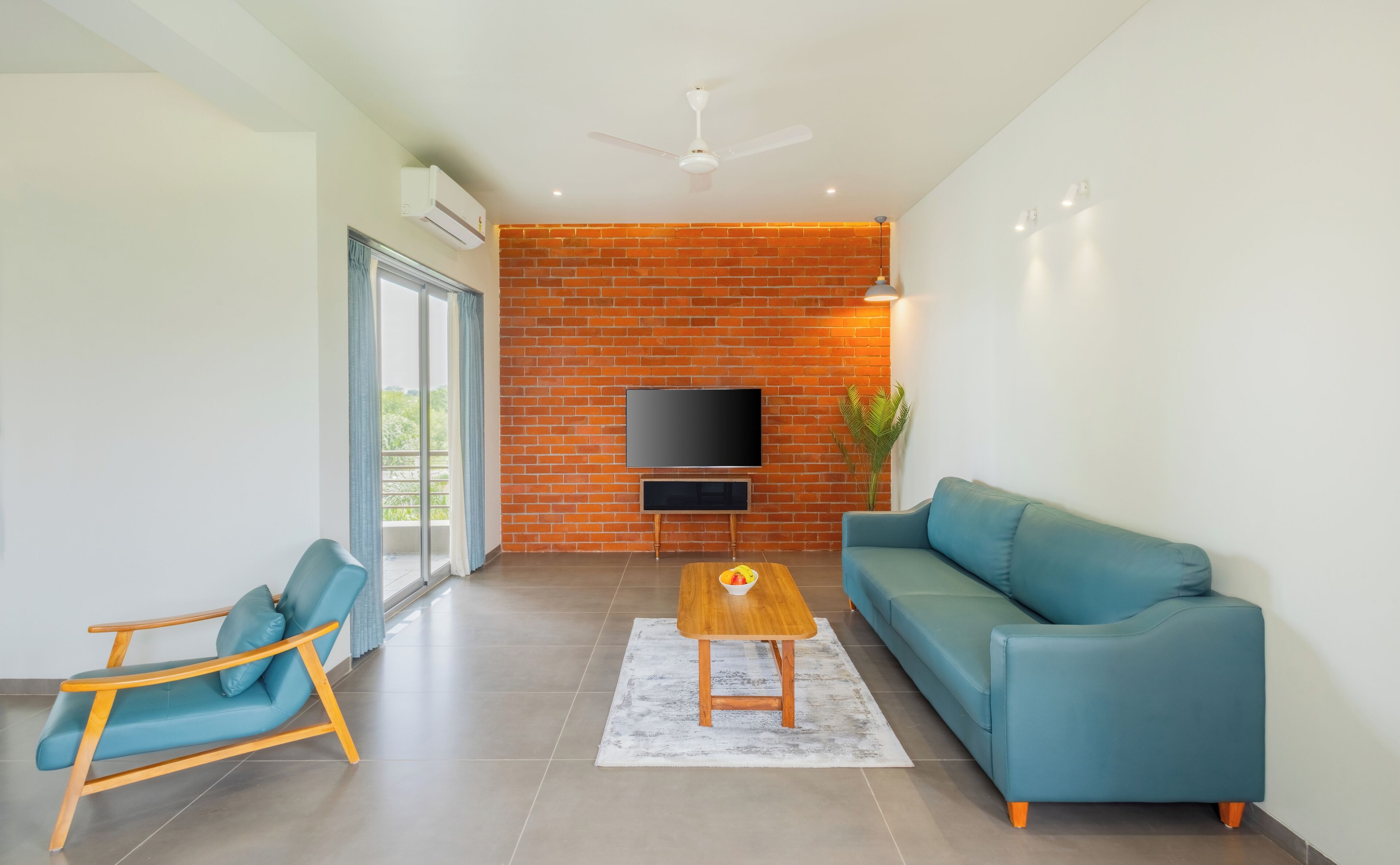 Una sala de estar moderna con pared de ladrillo, un televisor de pantalla plana, un sofá azul, una mesa de centro de madera y un sillón azul.