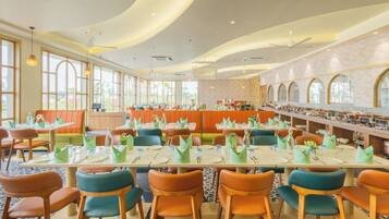 A spacious dining area with long tables, orange and teal chairs, and a central bar area.