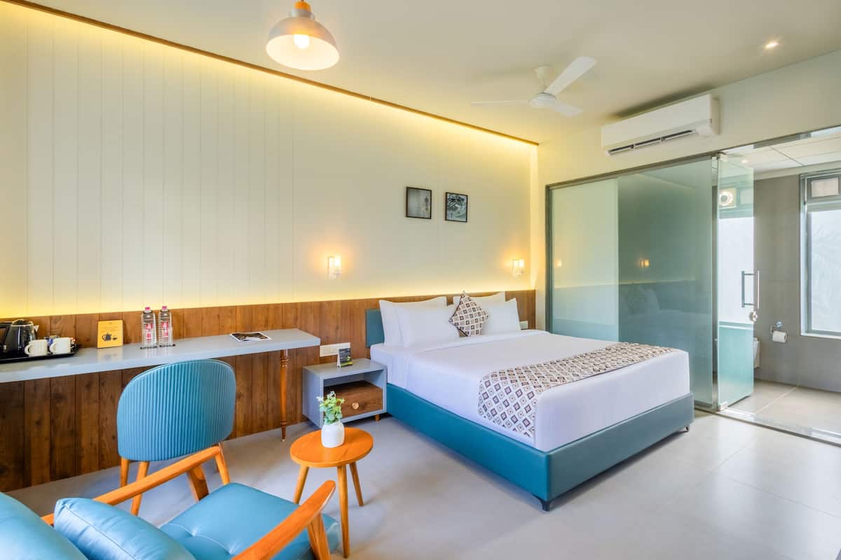 Quarto de hotel moderno com uma cama, uma escrivaninha, uma cadeira e uma mesinha.