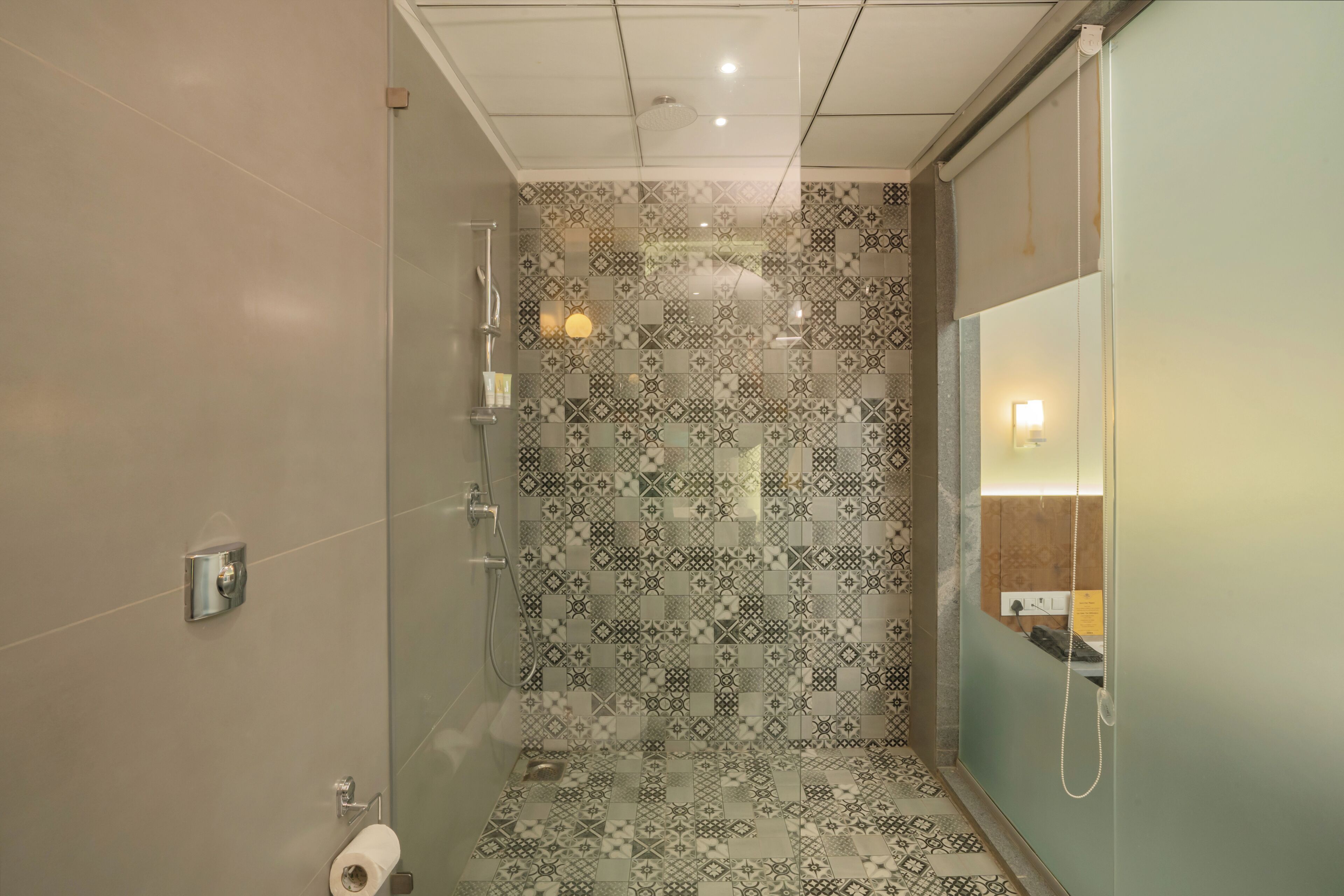 Un bagno moderno con piastrelle decorate, cabina doccia in vetro e uno specchio con illuminazione integrata.