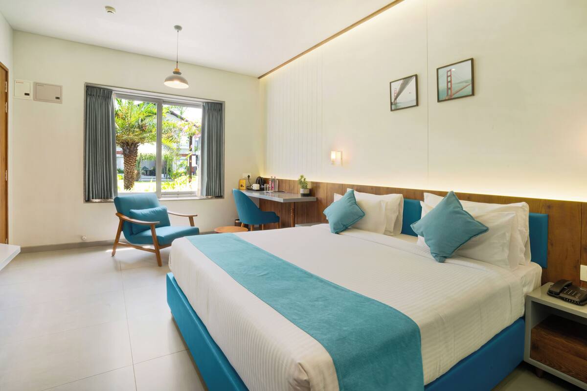 Quarto de hotel com uma cama grande, uma escrivaninha, uma cadeira e uma janela com cortinas.