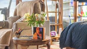 Une pièce chaleureuse avec une grande fenêtre, un canapé confortable, une petite table avec un livre et un vase de fleurs, et une couverture matelassée sur le lit.