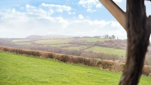Un paysage rural avec des collines douces, une haie et un bâtiment situé au loin.