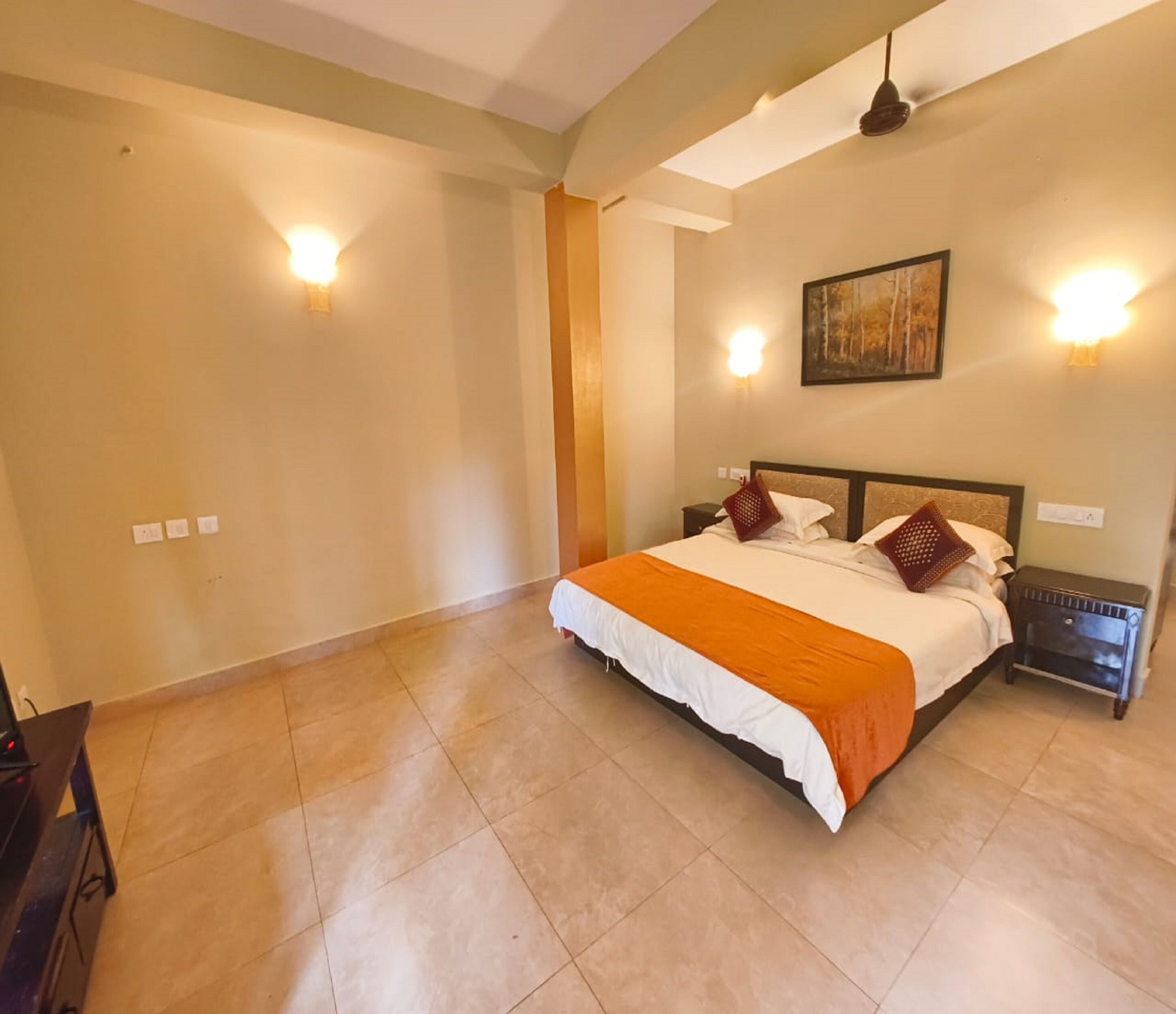 A spacious bedroom with a large bed, two bedside tables, and wall-mounted lights.