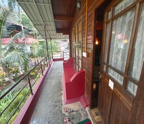 Un edificio de madera con un balcón cubierto, un banco rojo y una puerta con un letrero de número.