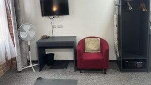 A compact room with a desk, a chair, a TV, a fan, a small trash bin, and a wardrobe. - Studio - Sleeps 2 - Parking - Wifi (Nottingham)
