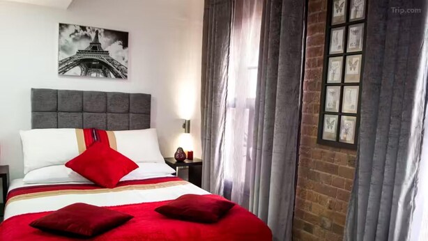 A hotel room with a large bed, a nightstand with a lamp, a window with curtains, and a picture of the Eiffel Tower on the wall. - Studio - Sleeps 2 - Parking - Wifi (Nottingham)