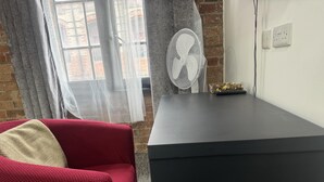 A room with a red sofa, a black desk, a white fan, and a brick wall. - Studio - Sleeps 2 - Parking - Wifi (Nottingham)