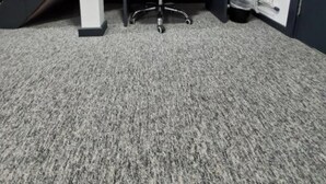Une pièce recouverte de moquette, avec un mur à rayures noires et blanches, un fauteuil de bureau noir, un bureau et un porte-manteau sur lequel est accroché un manteau.