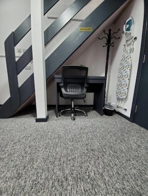 Una habitación con alfombra, una pared a rayas blancas y negras, una silla de oficina negra, un escritorio y un perchero con abrigo.