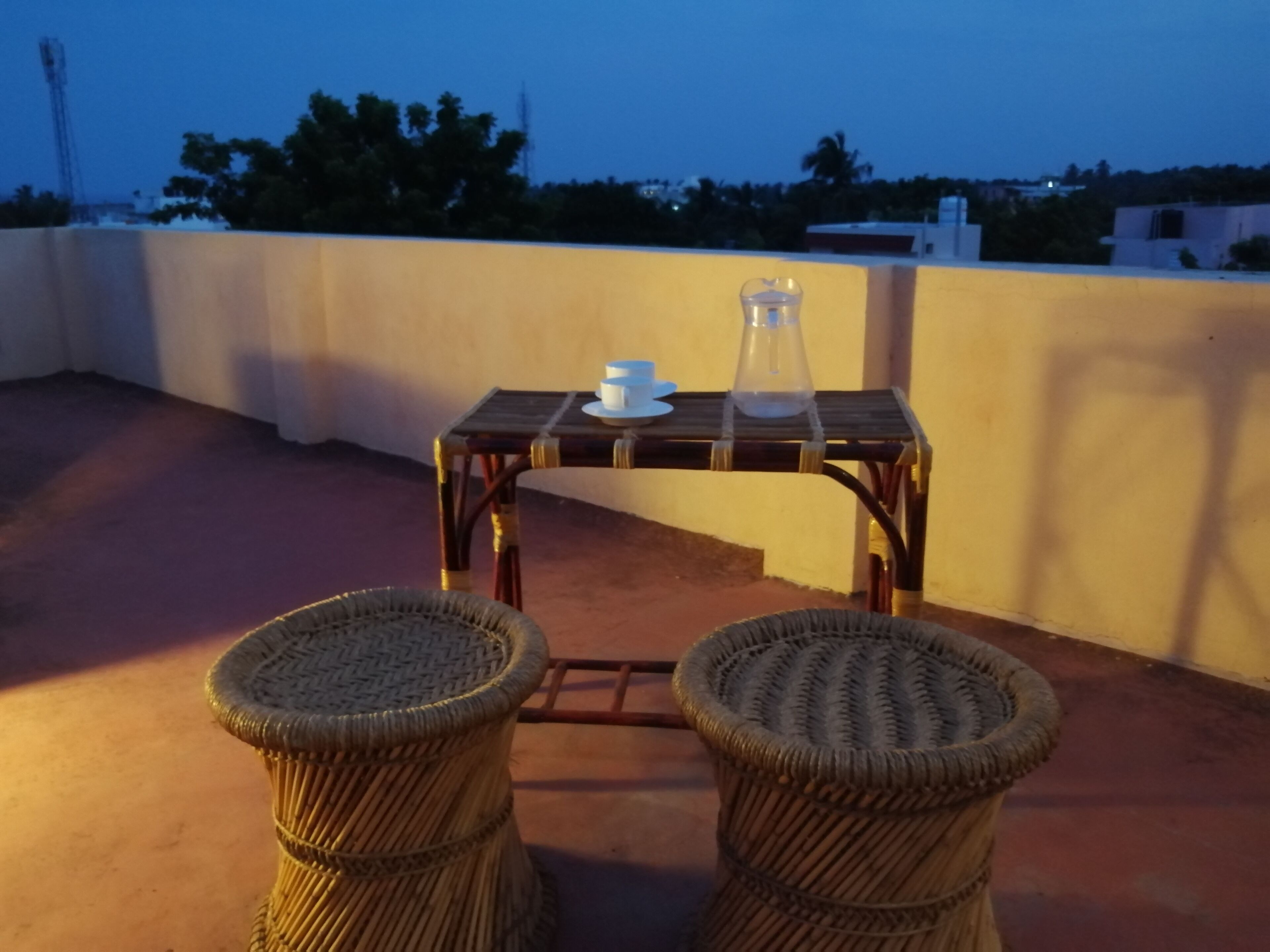 Una terrazza sul tetto con due poltrone in vimini, un tavolino e un boccale di vetro.