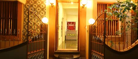Entrada de un hotel con una escalera, una reja metálica y un letrero que dice "Le Apex".
