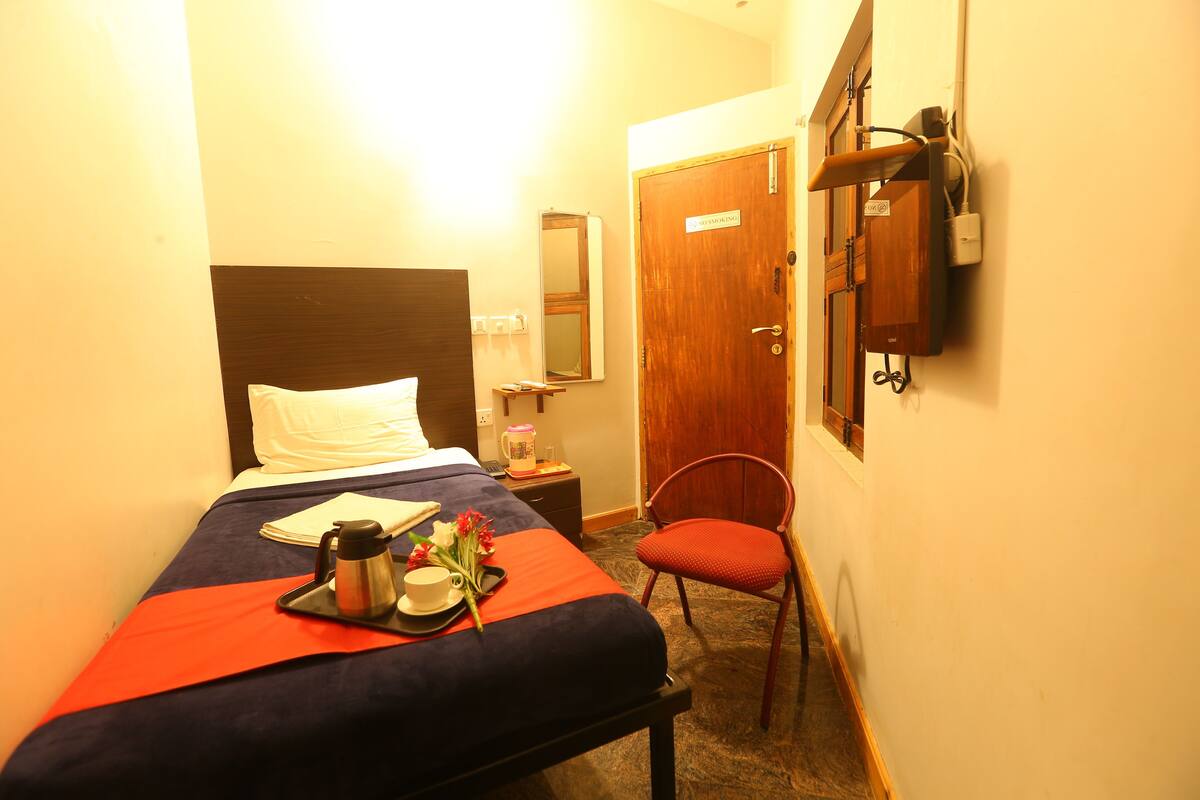 Une chambre d’hôtel avec un lit, une chaise, une table de chevet avec une lampe, un miroir et une porte.